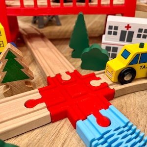 May include: A wooden toy train track set with a red bridge, a yellow taxi, a green tree, and a blue water track piece.
