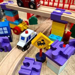 May include: A wooden toy train track set with a red toy car, a blue toy police car, a yellow toy train sign, and various colorful wooden blocks.