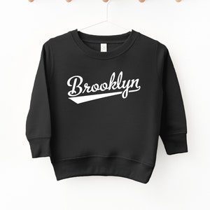 May include: Black sweatshirt with white text that says "Brooklyn" in a baseball-style font.