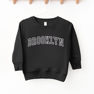 May include: Black sweatshirt with white text that reads "BROOKLYN" in a collegiate font.