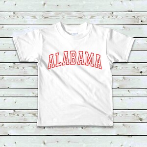 May include: White t-shirt with red text that says "ALABAMA" in a collegiate font.