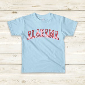 May include: A light blue t-shirt with the word "ALABAMA" printed in red on the front.