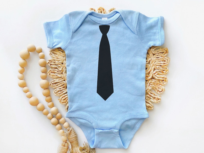 Op de afbeelding: Een lichtblauwe baby romper met een zwarte stropdas print op de voorkant.