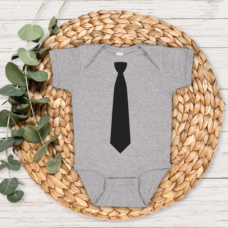 Op de afbeelding: Een grijze baby romper met een zwarte stropdas afbeelding op de voorkant.