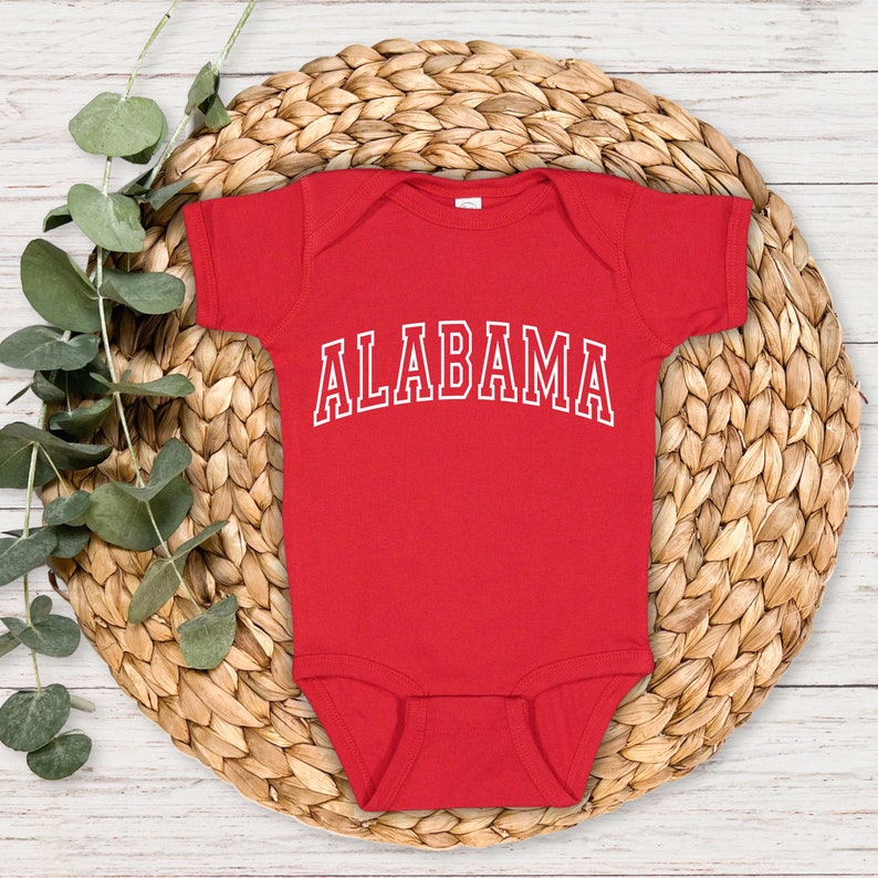 May include: Red baby onesie with white text that reads "ALABAMA" in a collegiate font.