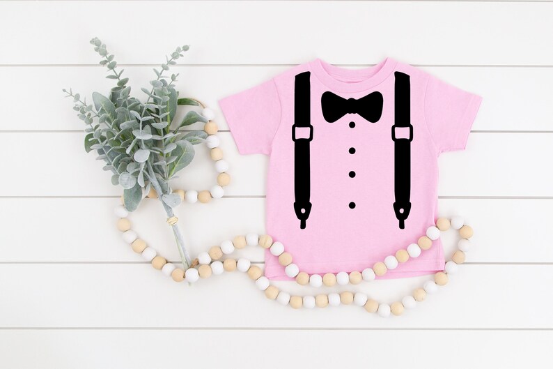 May include: A pink baby onesie with a black bow tie and suspenders graphic.