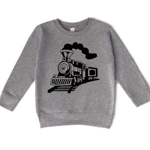 May include: A gray sweatshirt featuring a black illustration of a steam train with smoke billowing from the smokestack. The train is depicted on a track. The sweatshirt has long sleeves and a crew neck.