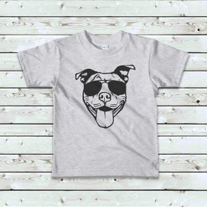 May include: A gray t-shirt with a black and white illustration of a dog wearing sunglasses. The dog is smiling and has its tongue sticking out.