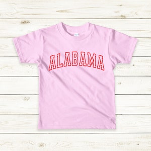 May include: A pink t-shirt with the word "ALABAMA" printed in red on the front.