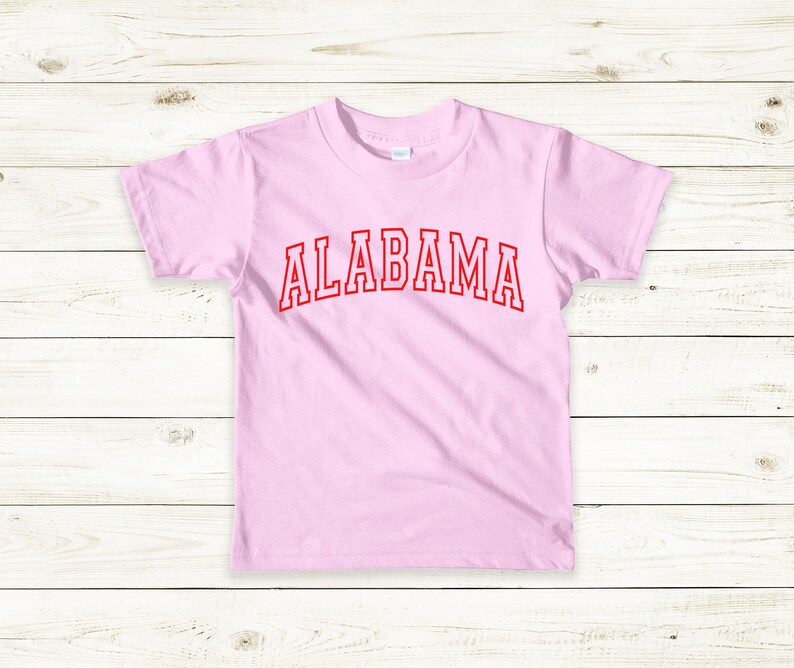 May include: A pink t-shirt with the word "ALABAMA" printed in red on the front.