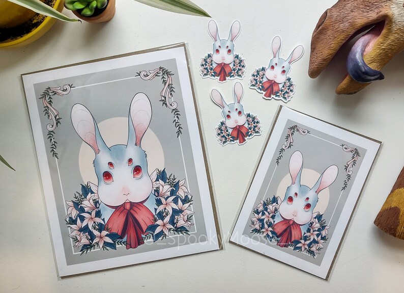 May include: A set of four prints featuring a white rabbit with red eyes and a red bow. The rabbit is surrounded by white flowers and green leaves. The prints are on a white background with a gray border.
