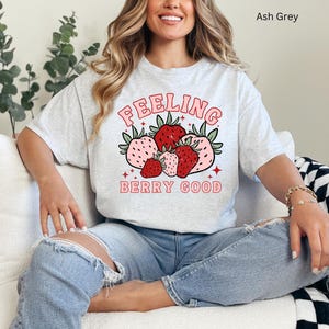 May include: A light gray t-shirt with a graphic of strawberries and the text "Feeling Berry Good".