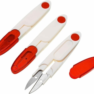 Könnte beinhalten: Drei Paar kleine, rote und weiße Nähscheren mit einer spitzen Spitze. Die Scheren haben einen weißen Kunststoffgriff mit einem roten Kreis oben. Die Klingen sind aus Metall und scharf.
