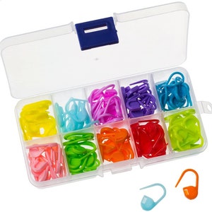 Könnte beinhalten: Eine transparente Plastik-Aufbewahrungsbox mit 10 Fächern, gefüllt mit bunten Plastik-Maschenmarkierern. Die Box hat einen blauen Verschluss. Es gibt auch drei lose Maschenmarker in den Farben Blau, Orange und Grün.