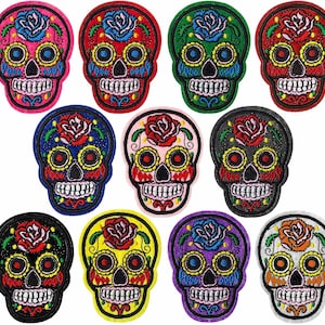 Könnte beinhalten: Eine Sammlung gestickter Sugar-Skull-Patches in verschiedenen Farben. Jeder Patch zeigt ein detailliertes Totenkopf-Design mit einer Rose. Farben sind Pink, Rot, Grün, Blau, Schwarz, Gelb und Lila. Die Patches eignen sich für Kleidung oder Accessoires.