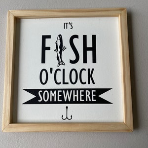 May include: A framed wood sign with white background and black text that reads "It's Fish o'Clock Somewhere" with a black silhouette of a fish and a fishing hook.