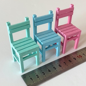 May include: Three miniature chairs in mint green, light blue, and pink, each featuring a slatted back and seat design. A metal ruler is positioned in the foreground, showing the chairs are approximately 9 to 10 cm in total height.
