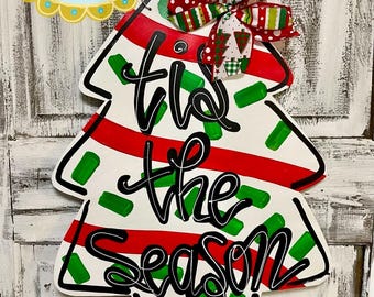 May include: A white wooden Christmas tree door hanger with red and green stripes, green polka dots, and the text "'tis the season".