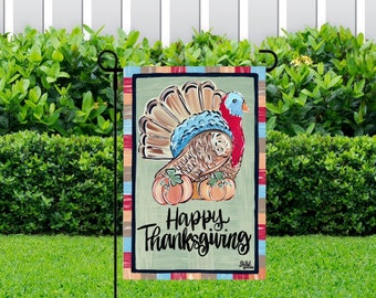 May include: A colorful garden flag with a Thanksgiving theme. It features a cartoon turkey with a blue and brown body, red wattle, and a brown tail. The turkey is surrounded by orange pumpkins. The flag has a green background with red, orange, and blue stripes around the border. The text "Happy Thanksgiving" is written in black cursive lettering.