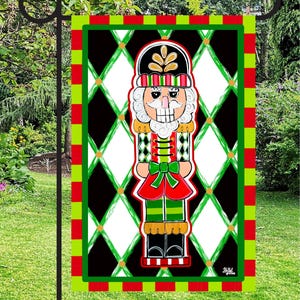 May include: A decorative Christmas garden flag featuring a colorful nutcracker design. The flag has a black and white diamond pattern background with a red, green, and black border. The nutcracker is dressed in red, green, and gold.