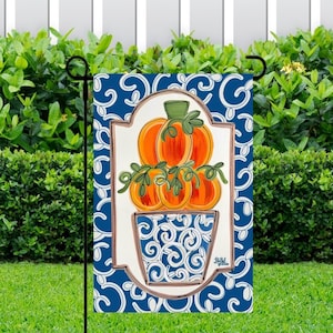 May include: A blue and white garden flag with a white frame and a design of orange pumpkins in a blue and white pot with a white swirl pattern. The pumpkins are stacked on top of each other and have green stems.