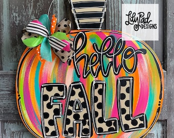 May include: A colorful pumpkin-shaped door hanger with the words "hello fall" in black lettering with black polka dots. The pumpkin is painted with swirls of orange, pink, blue, and green.