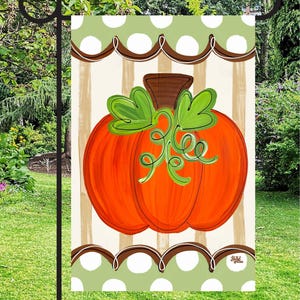 May include: A rectangular garden flag featuring a central orange pumpkin with a brown stem and green leaves. The background has vertical beige stripes, framed by top and bottom borders of light green with white polka dots and brown scalloped lines.