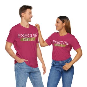 Puede incluir: Dos personas con camisetas rosas con el texto "EXECUTE EVERY DAY" en letras doradas y blancas. Las camisetas son un conjunto a juego.