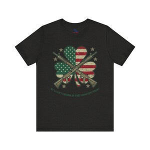 May include: Black t-shirt with a green four-leaf clover design. The clover has an American flag in the center and two crossed rifles. The text "My lucky charm is the constitution!" is printed below the clover.