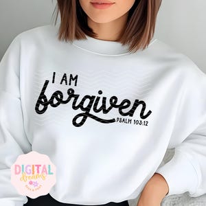 Könnte beinhalten: Weißer Pullover mit schwarzem Text, der "Ich bin vergeben" und "Psalm 103:12" lautet.