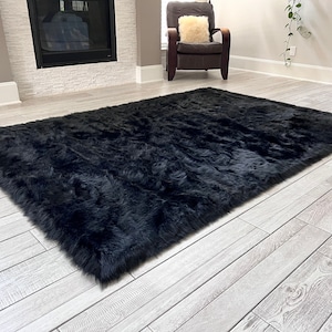 May include: A black faux fur rug with a long pile. The rug is laid out on a light wood floor.