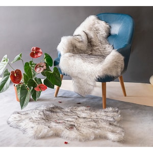 May include: A white faux fur throw rug with a blue armchair and a potted plant with red flowers in the background.