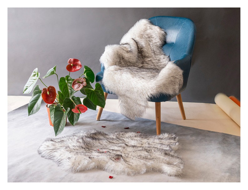 May include: A white faux fur throw rug with a blue armchair and a potted plant with red flowers in the background.