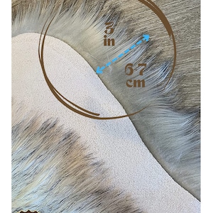 May include: Close-up of a light gray faux fur fabric with a 3 inch by 6.7 cm measurement marked on it.