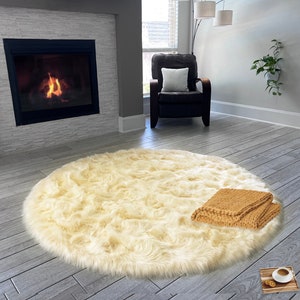 May include: A fluffy white faux fur rug with a brown knitted throw blanket on top. The rug is in a living room setting with a fireplace and a chair.