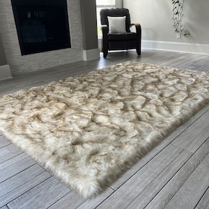 Puede incluir: Una alfombra de piel sintética blanca y marrón esponjosa con una pila larga. La alfombra está colocada sobre un suelo de madera gris claro.