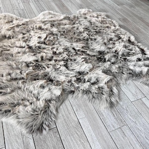 May include: A large, fluffy, gray and white sheepskin rug. The rug has a natural, shaggy texture and is perfect for adding warmth and comfort to any room.