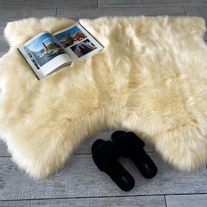May include: A cream-colored faux fur rug with a book lying on top of it. Two black slippers are on the rug.