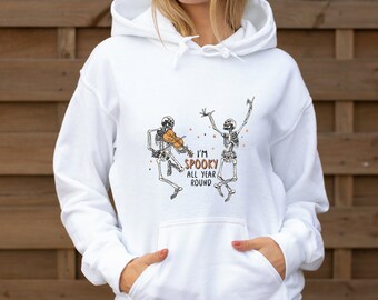 Peut inclure: Sweat-shirt à capuche blanc avec un motif de deux squelettes, l'un jouant du violon. Le texte dit "I'm Spooky All Year Round".