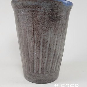 May include: A handmade ceramic vase with a textured, ridged exterior. The vase has a dark gray-brown body with a blue rim. The bottom of the vase is a darker shade of gray. The number "6268" is printed in white on the bottom right.
