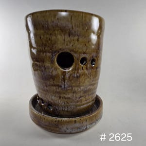 May include: A handcrafted ceramic planter with a brown and white glaze. The cylindrical pot features a large central hole and several smaller holes, with a matching saucer base. The number "# 2625" is printed on the bottom right.