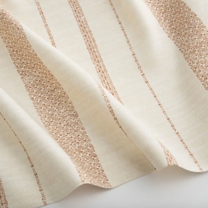 以下が含まれることがあります： クリーム色の生地のクローズアップ。さまざまな幅とパターンで垂直ストライプが施されています。ストライプは、無地の線と、温かみのある茶色の詳細な幾何学模様の間で交互に表示されます。生地はわずかにドレープされています。