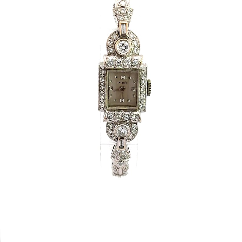 Op de afbeelding: Een vintage polshorloge met een vierkante wijzerplaat en een band bezet met diamanten. De wijzerplaat is wit met zwarte Romeinse cijfers als uurmarkeringen en het woord "LATEMINE" staat in het zwart gedrukt.
