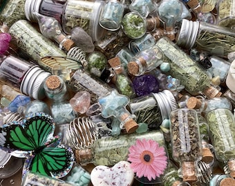 May include: A collection of small glass bottles filled with various dried herbs, crystals, and other natural elements. The bottles have cork tops and are arranged in a wooden bowl.