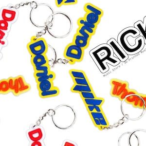 May include: A collection of colorful, 3D printed keychains with names like "Daniel", "Thomas", "Mike", and "SowoyL". The keychains are on a white background. The text "RICK'S Music Store / 3D Printed Music Accessories / And More" is visible in the image.