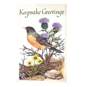 May include: A greeting card featuring the text Keepsake Greetings at the top. The illustration depicts an American robin with an orange breast perched on a branch above a fallen log, surrounded by purple thistle flowers and yellow daisies.