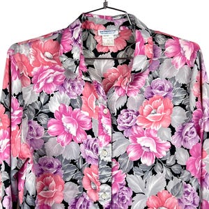 May include: A button-down blouse with a vibrant floral pattern in shades of pink, purple, and gray on a black background. The long-sleeved shirt features a classic collar and button closure. The tag reads "JONATHAN MARTIN & CO. SAN FRANCISCO, CA."