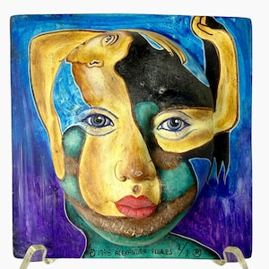 May include: A square ceramic wall plaque featuring a stylized, multi-faceted face with blue, yellow, and black tones. The artwork displays bright red lips, detailed blue eyes, and the text 1998 ALEXANDER FLURES 1/1 at the bottom edge.