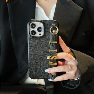 Peut inclure: Coque de téléphone en cuir noir avec une dragonne dorée. La dragonne porte le nom "LISA" en lettres dorées. L'étui a une surface texturée et un module caméra à trois objectifs.