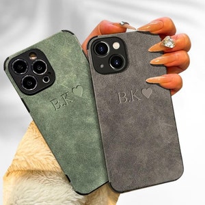 May include: Two phone cases with a suede-like texture. The cases are grey and green and have the initials "B.K." and a heart printed on them.